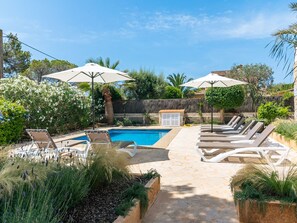 A swimming pool with lounge chairs and umbrellas, surrounded by greenery and a stone wall. - Villa Azul by Interhome (Santanyí)