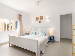 A bedroom with a white bed, two bedside tables with lamps, a window with curtains, and a wall-mounted light fixture. - Villa Azul by Interhome (Santanyí)