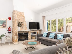 A living room with a stone fireplace, a flat-screen TV, a sofa with patterned cushions, and a coffee table with a decorative plate. - Villa Azul by Interhome (Santanyí)