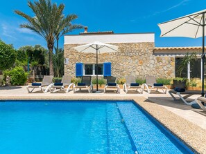 A poolside area with lounge chairs and umbrellas, a stone building with blue shutters, and a clear blue pool. - Villa Azul by Interhome (Santanyí)