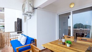 Un balcon avec une table en bois, des chaises, un canapé bleu et un appareil de climatisation.