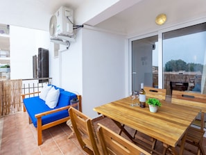 Ein Balkon mit Holztisch, Stühlen, einer blauen Couch und einer Klimaanlage.