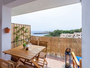 A wooden table and chairs on a balcony with a view of the sea and buildings. - Apartment  by Interhome (Portocolom)