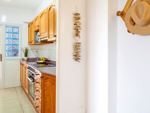 A kitchen with wooden cabinets, a granite countertop, and a hanging decorative piece. - Apartment  by Interhome (Portocolom)