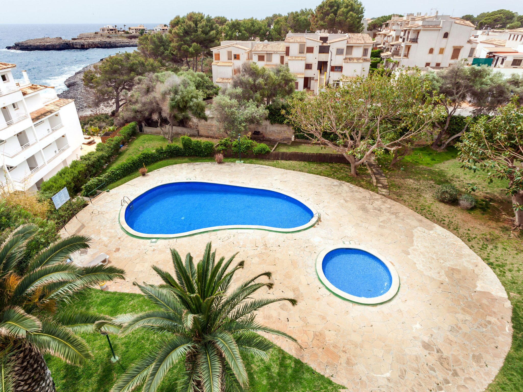 A residential area with a swimming pool, lush greenery, and a view of the sea.