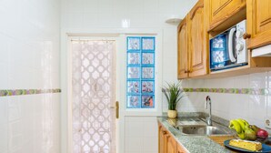 Une cuisine avec des carreaux blancs, des meubles en bois, un évier en acier inoxydable et une fenêtre aux montants bleus.