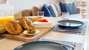Une table dressée pour le petit-déjeuner avec des croissants, du fromage, des olives et un verre de jus d’orange, le tout disposé sur une planche en bois.