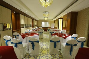 Un salón de banquetes con mesas redondas, sillas blancas con cintas azules y una gran lámpara de candelabro.