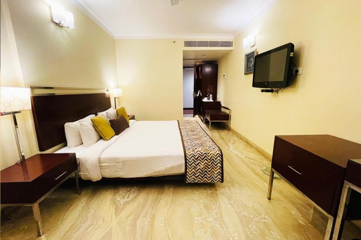 A hotel room with a bed, bedside tables, a desk, a chair, a TV, and a wardrobe.