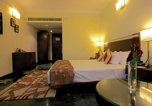 Una habitación de hotel con una cama, mesita de noche, lámpara y un jarrón con una flor.