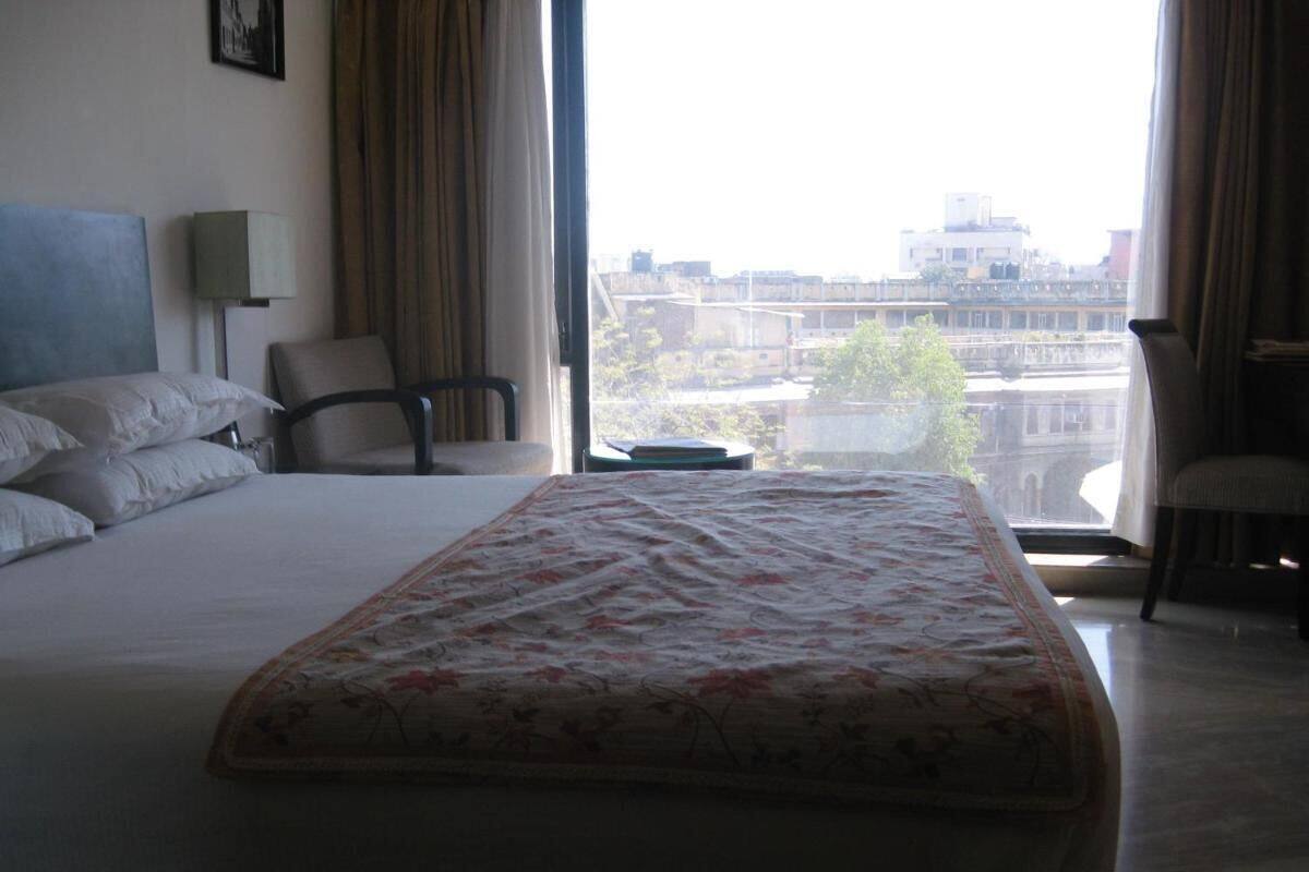 A hotel room with a large bed, a chair, a desk, and a view of buildings through the window.