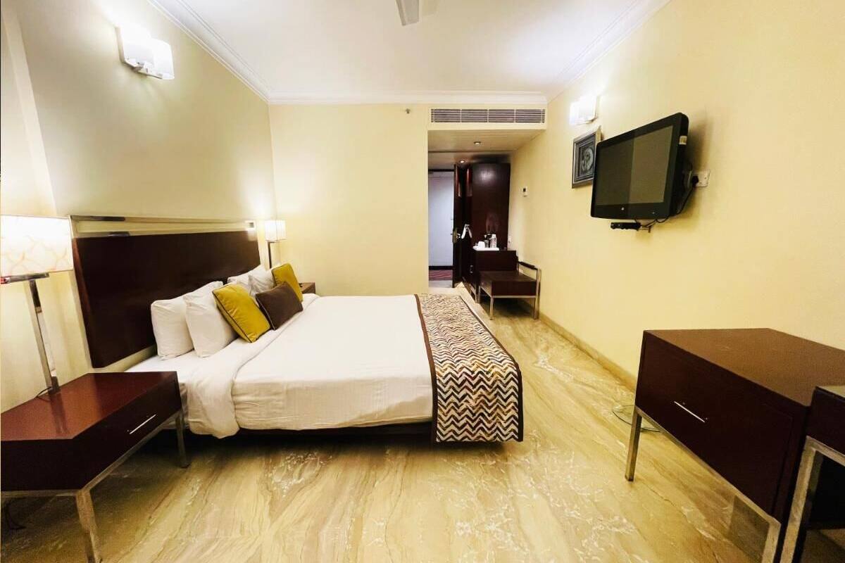 A hotel room with a bed, bedside tables, a desk, a chair, a TV, and a wardrobe.