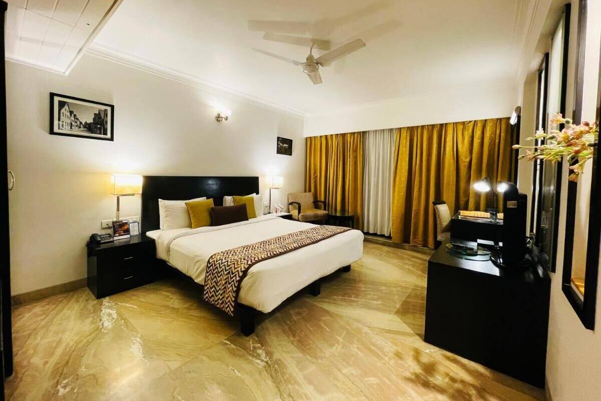 A hotel room with a bed, nightstands, a desk, a ceiling fan, and curtains.