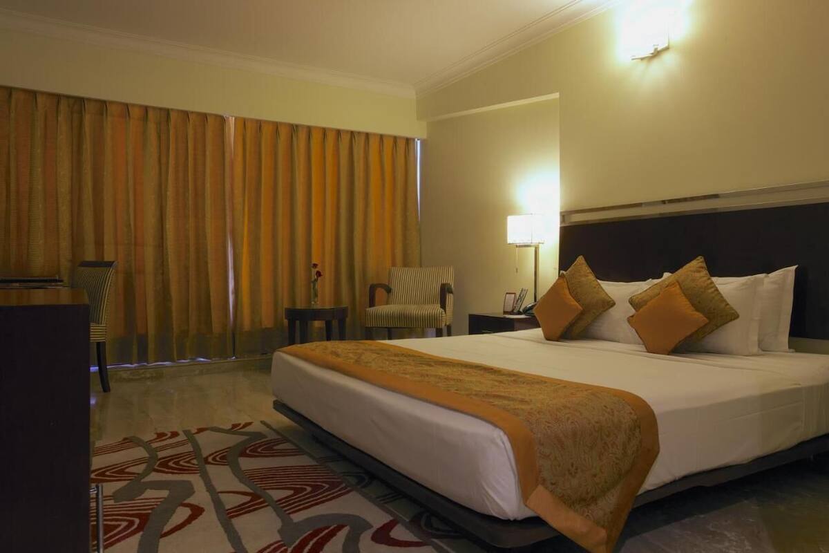 A hotel room with a large bed, a desk, a chair, a lamp, and a window with curtains.