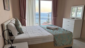 A bedroom with a bed, a bedside table, a lamp, a dresser, and a view of the sea. - Amazing 4-bedroom seafront villa with infinity pool in Kalkan (Kaş)