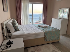 A bedroom with a bed, a bedside table, a lamp, a dresser, and a view of the sea. - Amazing 4-bedroom seafront villa with infinity pool in Kalkan (Kaş)