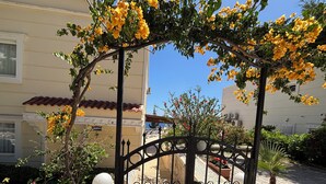 A gated entrance with a wrought iron gate, a potted plant, and a stone pathway leading to a building with a tiled roof. - Amazing 4-bedroom seafront villa with infinity pool in Kalkan (Kaş)