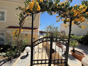 A gated entrance with a wrought iron gate, a potted plant, and a stone pathway leading to a building with a tiled roof. - Amazing 4-bedroom seafront villa with infinity pool in Kalkan (Kaş)