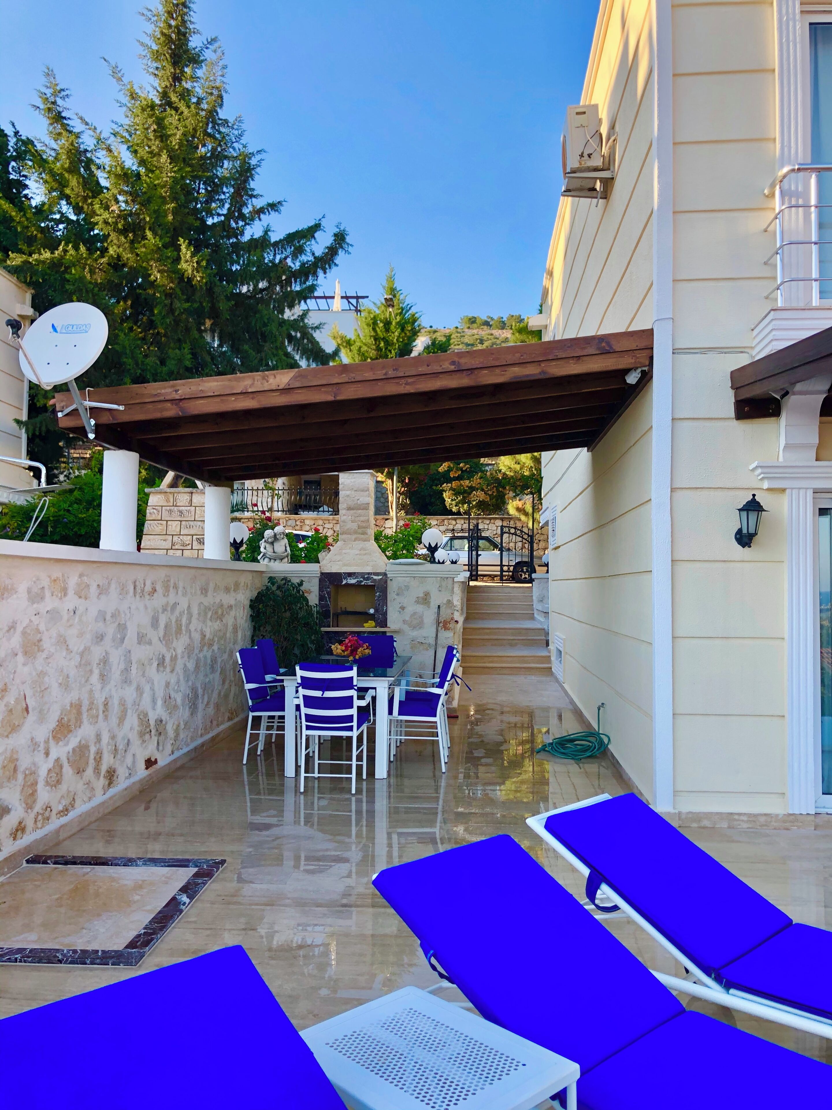 Une terrasse extérieure couverte, dotée d’un mur en pierre, d’un barbecue et d’un espace repas avec des chaises et une table.