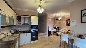 A modern kitchen with a gas stove, oven, and white cabinets. There is a dining area with a table and chairs. - Amazing 4-bedroom seafront villa with infinity pool in Kalkan (Kaş)
