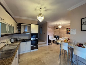 A modern kitchen with a gas stove, oven, and white cabinets. There is a dining area with a table and chairs. - Amazing 4-bedroom seafront villa with infinity pool in Kalkan (Kaş)