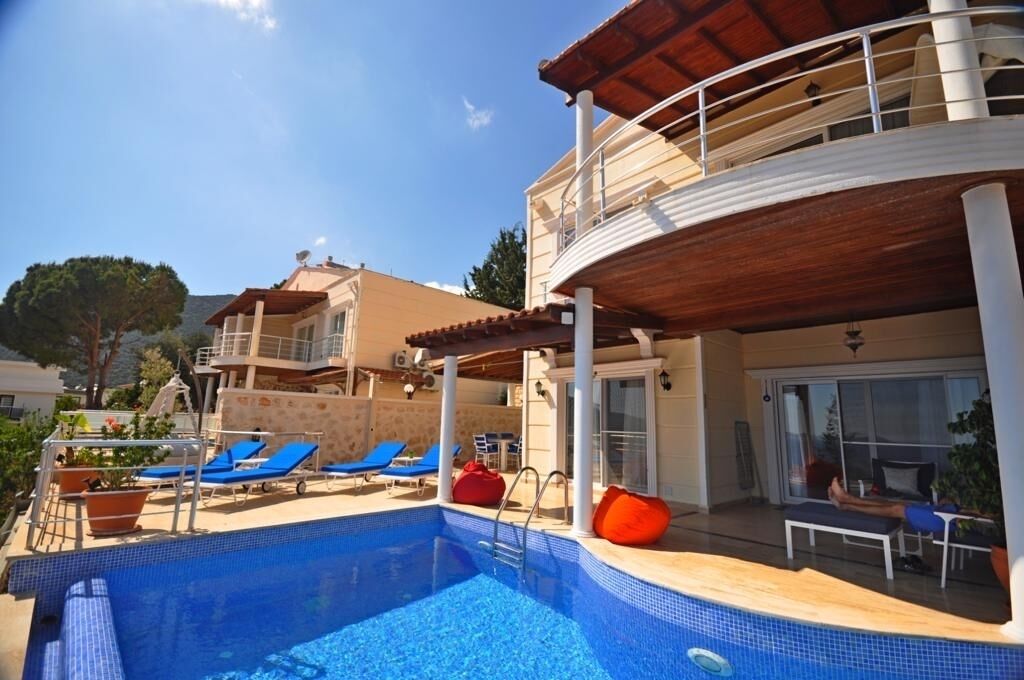 Uma área de piscina com espreguiçadeiras, um assento saco vermelho e um edifício com varanda.