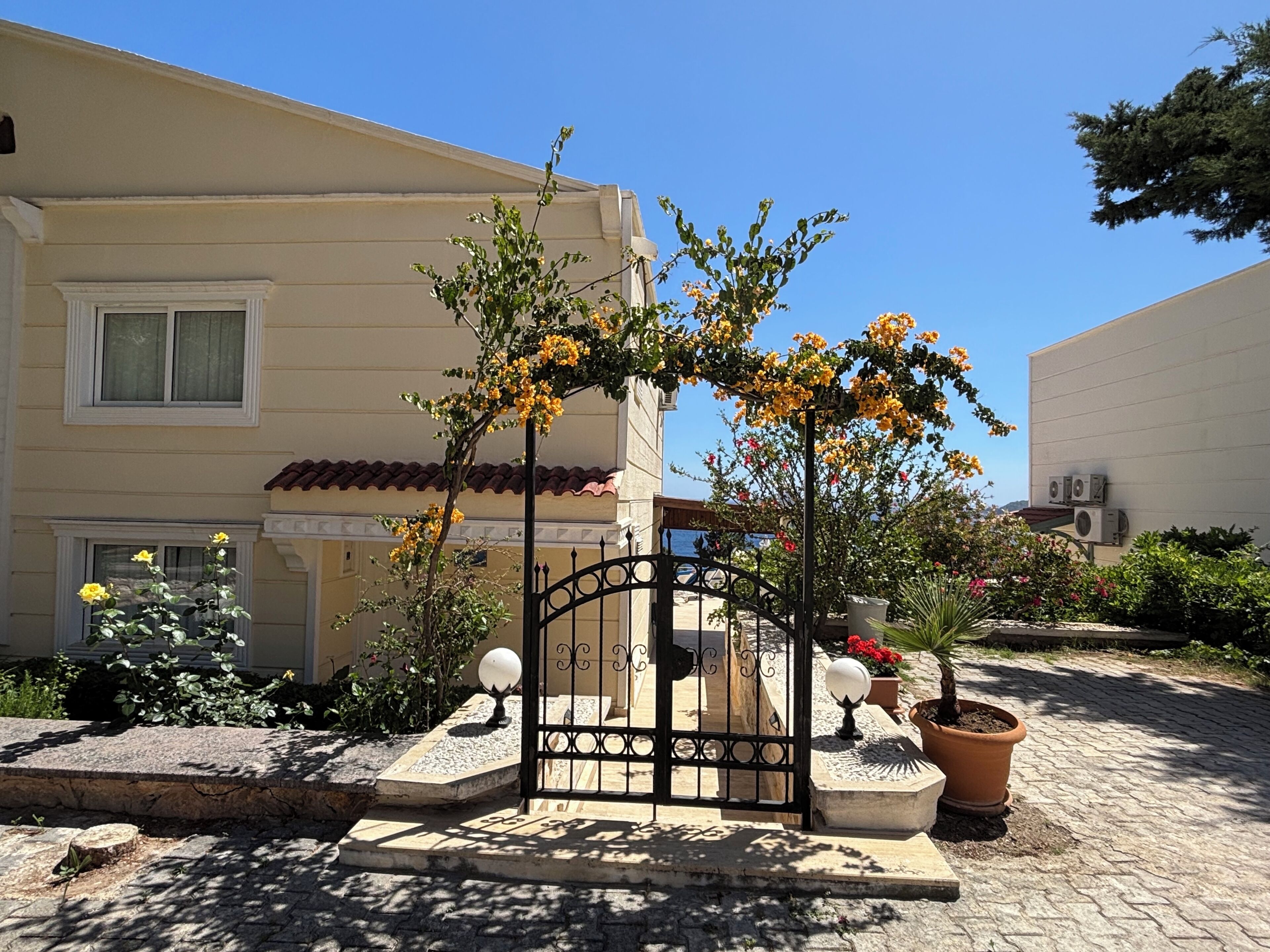 A building with a gated entrance, potted plants, and a clear sky.