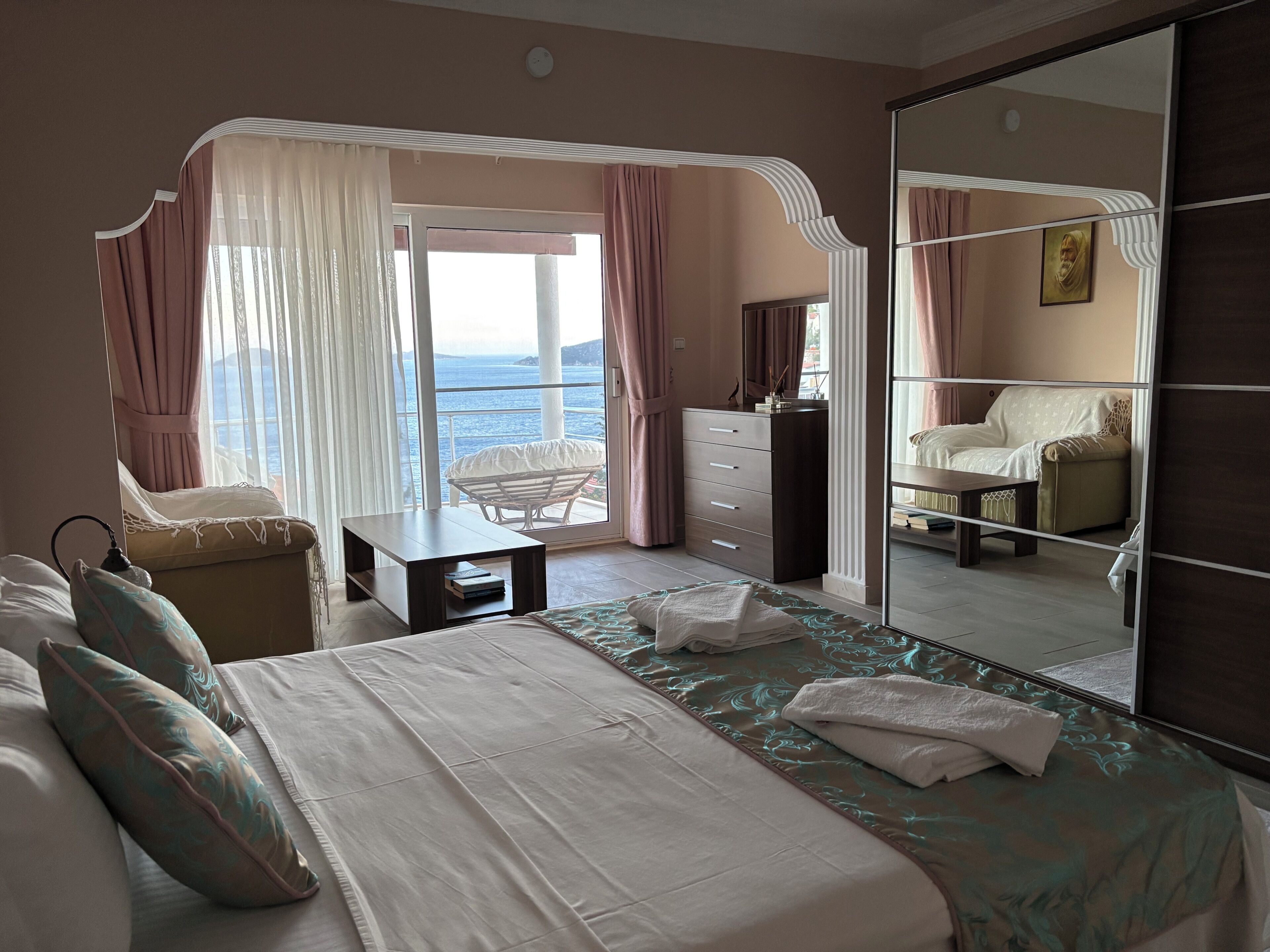 A hotel room with a bed, a desk, a chair, a dresser, and a large mirror reflecting the room.
