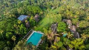 An aerial view of a resort with a swimming pool, thatched-roof structures, and dense tropical vegetation. - Marari Beach Resort - A CGH Earth Experience (Cherthala)