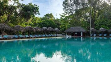 A swimming pool with lounge chairs and thatched-roof structures.