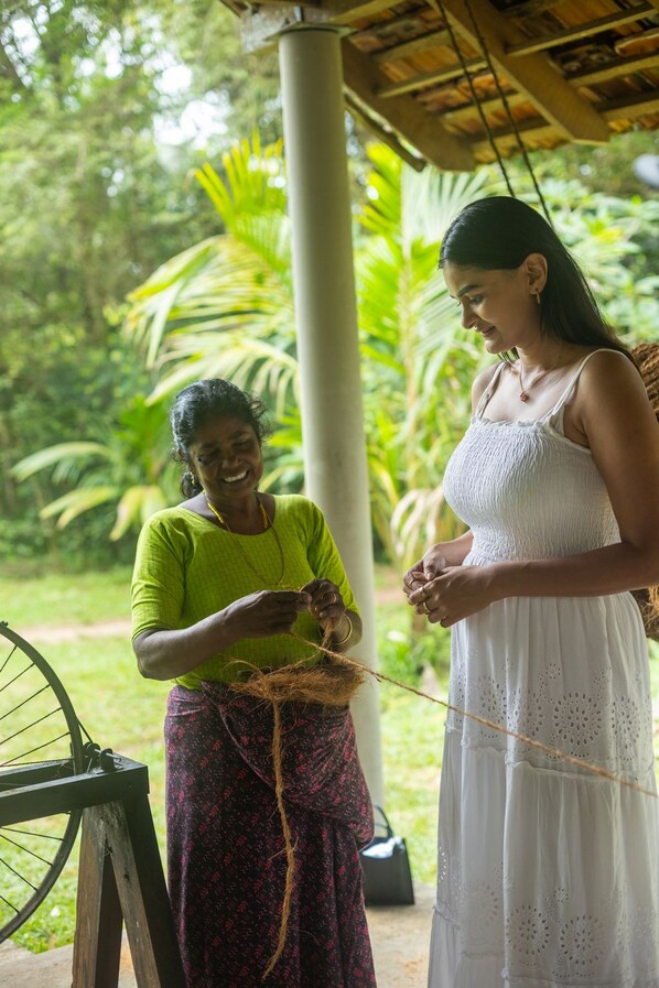 Two individuals engaged in an activity outdoors, with a structure overhead and greenery in the background. - Marari Beach Resort - A CGH Earth Experience (Cherthala)