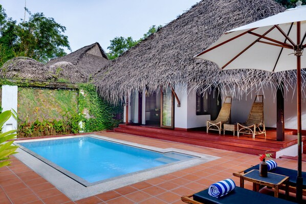 A poolside area with a thatched-roof structure, lounge chairs, and a tiled pool.