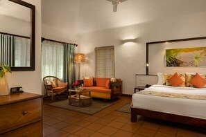 A hotel room with a bed, a sofa, a chair, a desk, a lamp, and a painting on the wall.