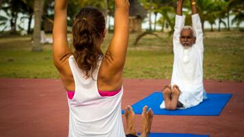 Two individuals practicing yoga on blue mats outdoors with palm trees in the background.