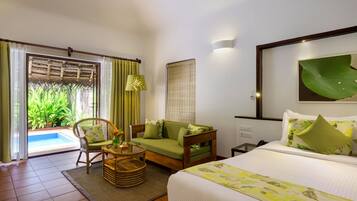 A hotel room with a bed, a sofa, a chair, a small table, and a view of a swimming pool.