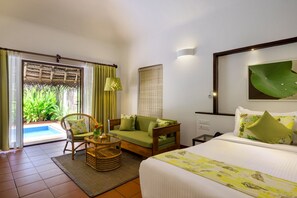 A hotel room with a bed, a sofa, a chair, a small table, and a view of a swimming pool.
