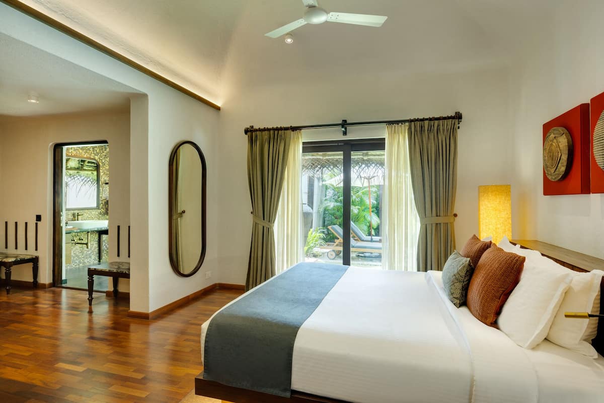 A hotel room with a large bed, a ceiling fan, a view of the outdoors, and a bathroom with a shower and sink.