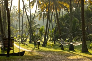 A pathway leading through a tropical garden with palm trees, hammocks, and a wooden structure. - Marari Beach Resort - A CGH Earth Experience (Cherthala)