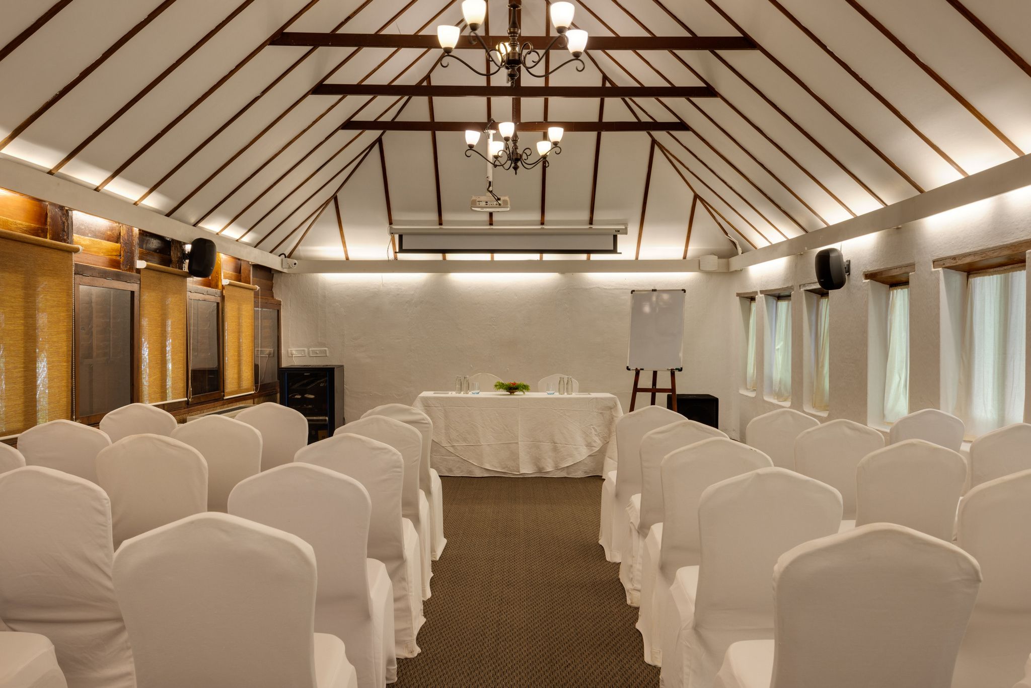 Una sala conferenze con sedie bianche, un tavolo con tovaglia bianca, un lampadario e pannelli di legno a soffitto.