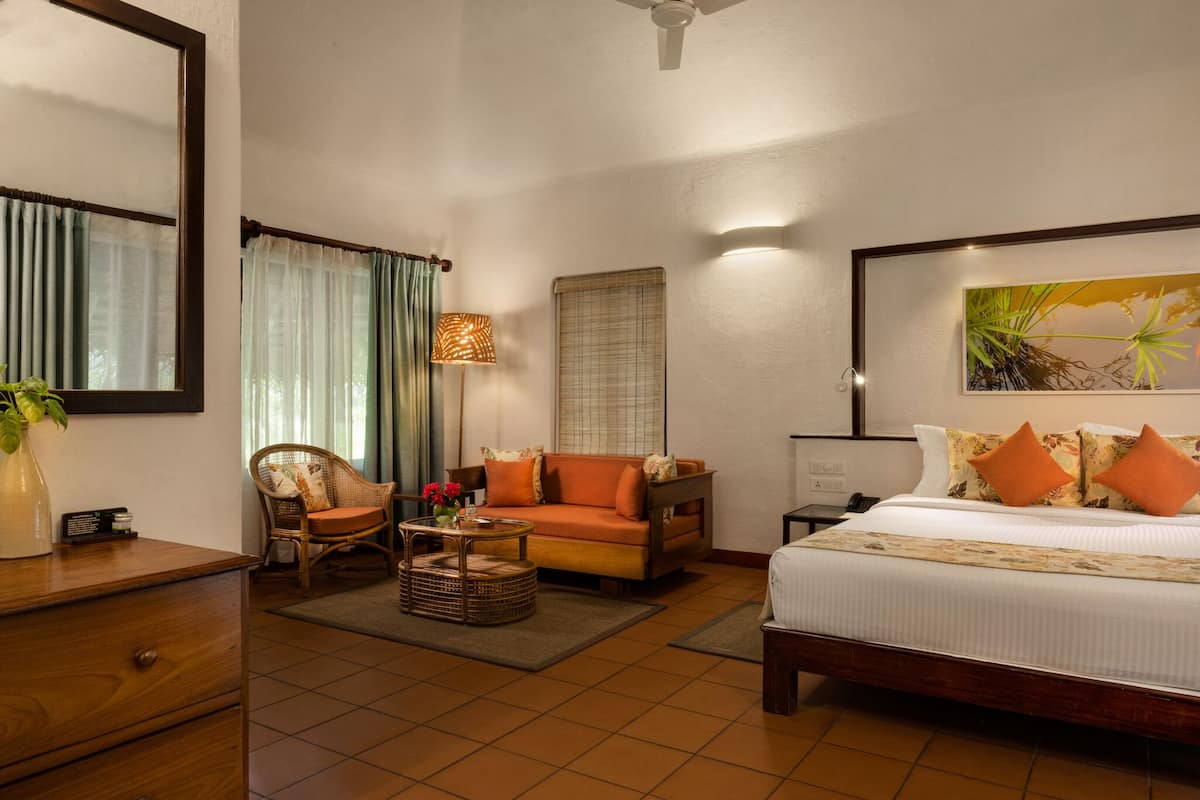 A hotel room with a bed, a sofa, a chair, a desk, a lamp, and a painting on the wall.