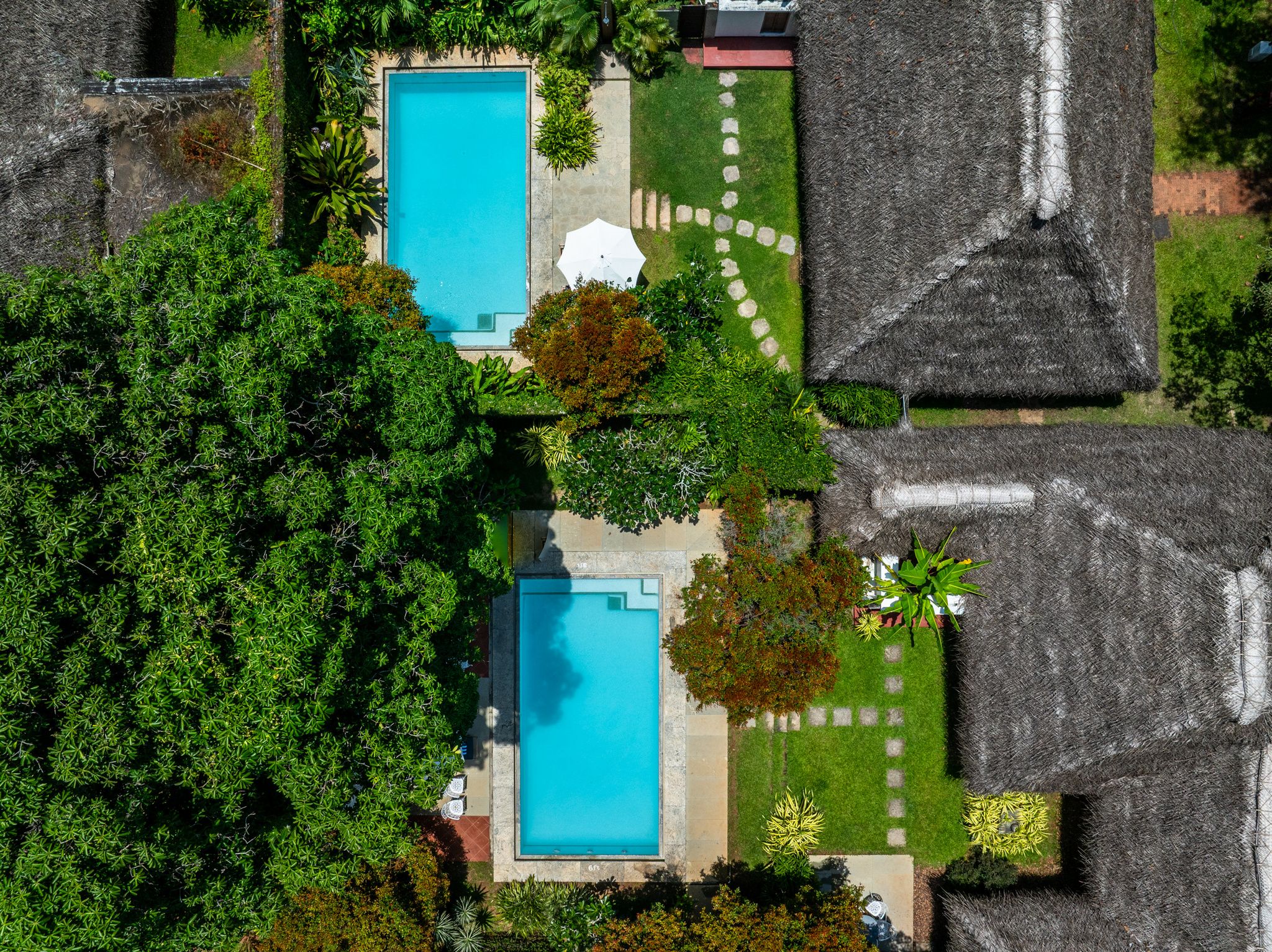 Vista aérea de uma propriedade com duas piscinas, rodeada por vegetação exuberante e construções com telhados de palha.