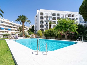 A swimming pool with two ladders, surrounded by greenery and a white building with balconies. - Apartment  by Interhome (Nerja)