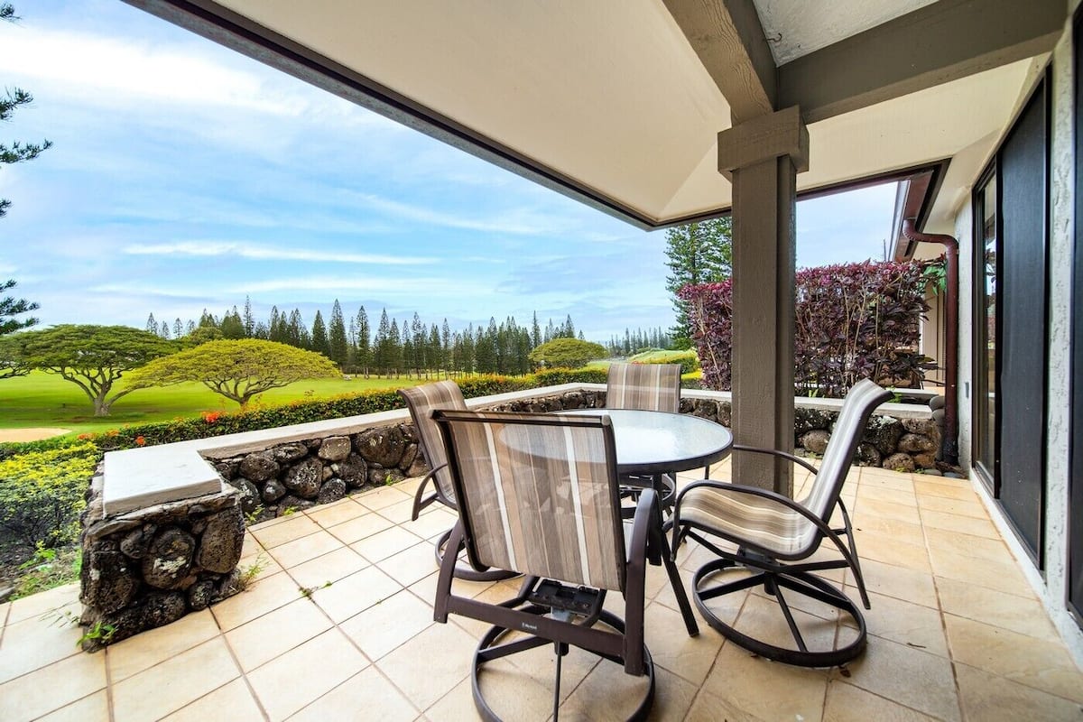 Eine überdachte Terrasse mit Tisch und Stühlen, eine Steinmauer und Blick auf einen angelegten Garten.