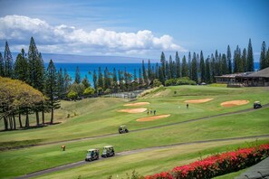 A golf course with a clubhouse, a road with golf carts, and a view of the ocean. - The Kapalua Villas Maui by Outrigger (KAPALUA)