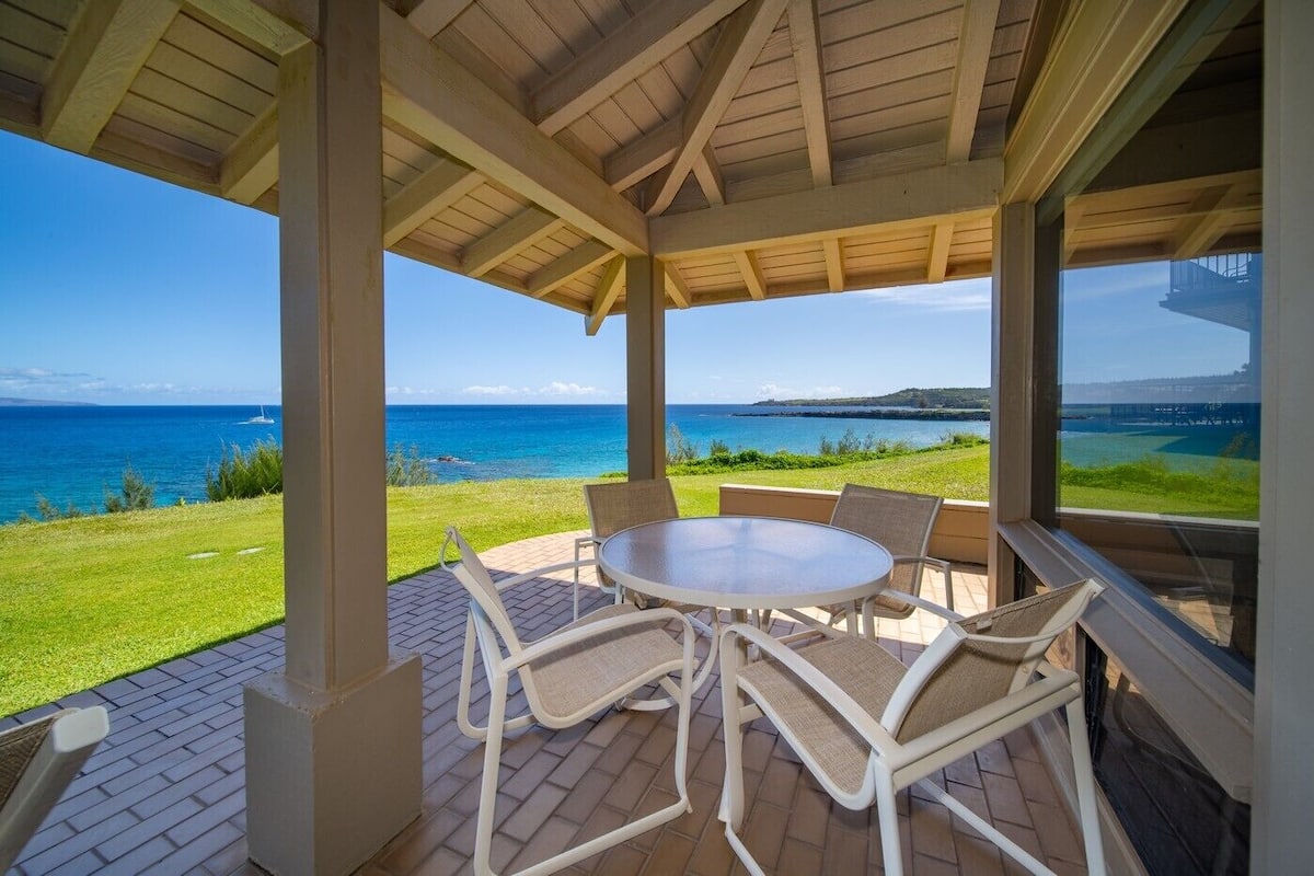 Ein überdachter Außenbereich mit Tisch und Stühlen, mit Blick auf eine grüne Landschaft und das Meer.