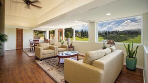 A spacious living room with a large window, a ceiling fan, and a dining area with chairs and a table. - The Kapalua Villas Maui by Outrigger (KAPALUA)