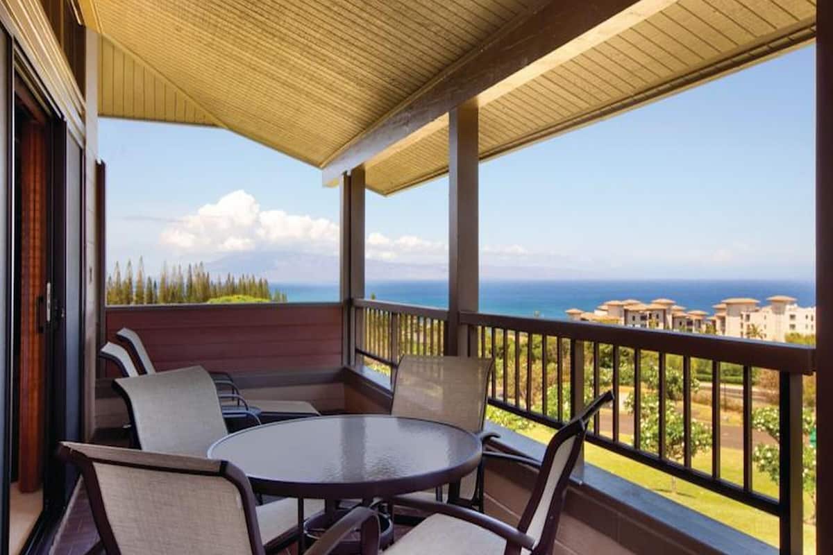 Ein überdachter Außenbereich mit Tisch und Stühlen, der einen schönen Blick auf das Meer und die Gebäude bietet.