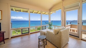 A spacious living room with a large window overlooking the ocean, a cozy sofa, a small round table, and a wooden floor. - The Kapalua Villas Maui by Outrigger (KAPALUA)