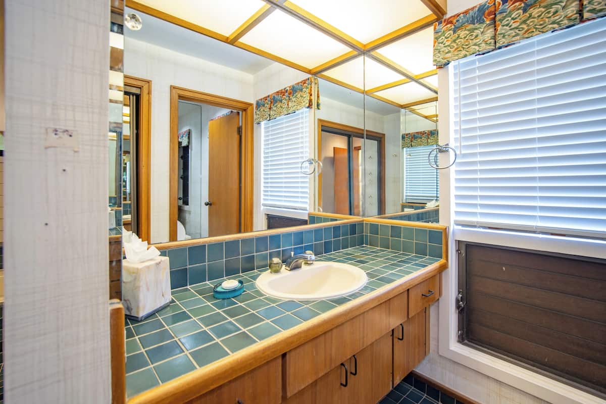 Ein Badezimmer mit Waschbecken, Spiegel und Fenster mit Jalousien.