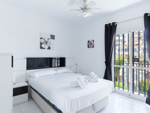 A modern bedroom with a large bed, white bedding, a ceiling fan, and artwork on the walls. - Los Pinos 25 Villas by Casasol by Interhome (Nerja)